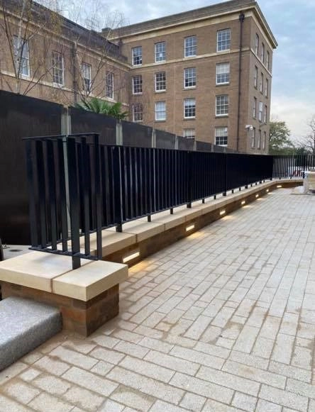 The railing is mounted on top of a retaining wall to prevent pedestrians from accidentally falling onto the lower brick walkway below.